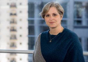 Dr. Quintana sits in front of a large window with buildings blurred in the background. She is wearing a blouse.