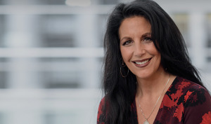 Dr. La Civita is sitting in front of a large window with a building blurred in the background. She is wearing a blouse.