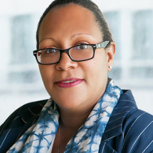 Dr. Dennis is sitting in front of a large window with a building blurred in the background. She is wearing a blouse and blazer.