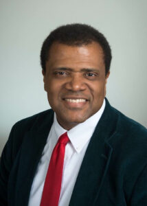 Dr. Kablo is sitting in front of a professional colored backdrop. He is wearing a suit and tie.