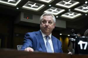 CSIS Director dressed in a blue suit, sitting behind a desk with a pensive look on his face.