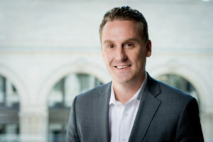 Man siting in front of building wearing a suit jacket