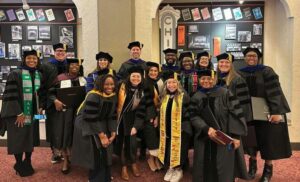 Kimberely at graduation in her cap and gown with a group of 10 other graduating students dressed in regalia.