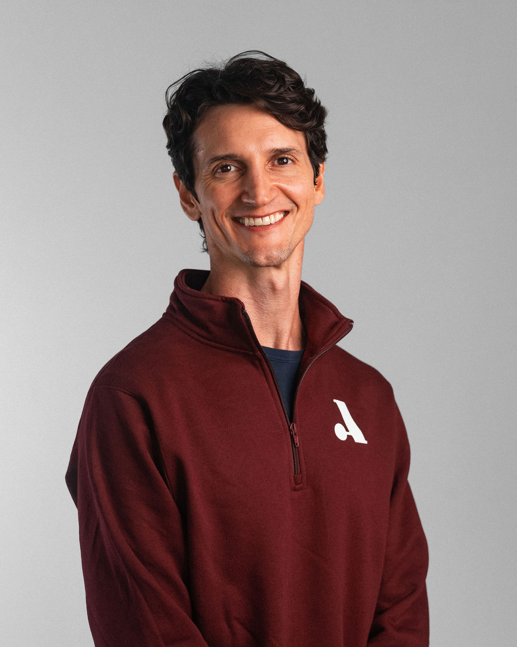 Zach Twardowski, a man with short brown hair, stands and smiles in a maroon pullover with a white logo against a plain gray background.