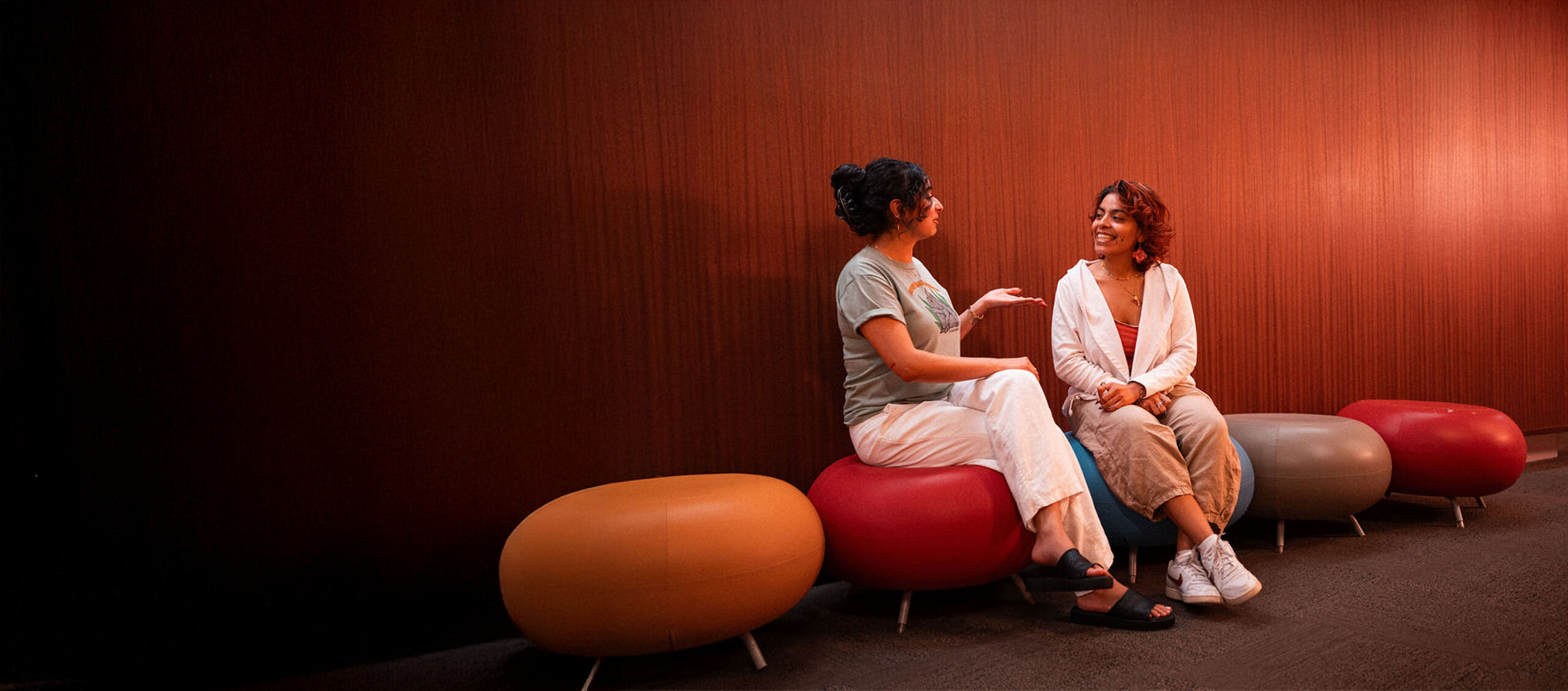 Two Adler Univeristy students sitting on round colorful stools conversing