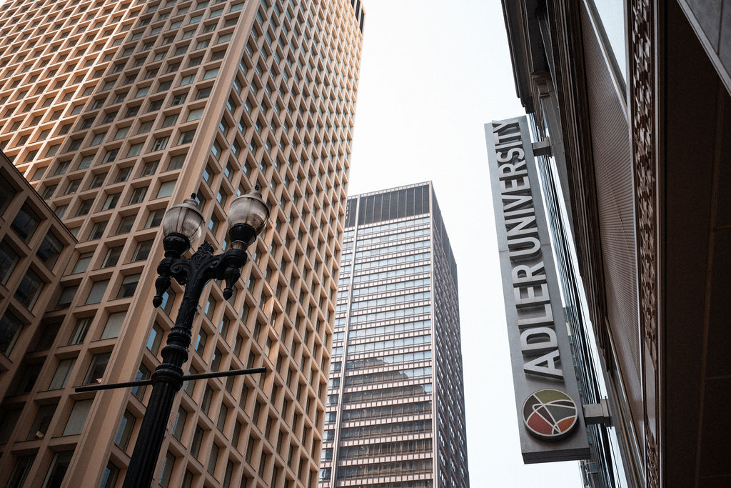 View looking up at tall office buildings in a city, with a streetlamp and an Adler University sign on the right side of the image.