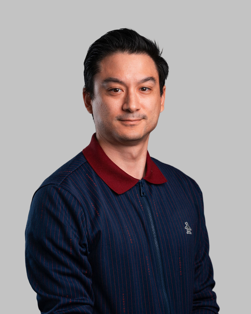 Daniel Katz, a man with short dark hair, wears a navy pinstripe jacket with a maroon collar as he poses against a plain grey background.