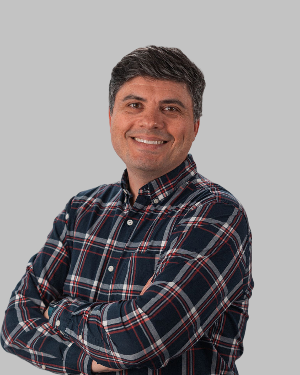 Filipe Ramos, a man with short dark hair, stands against a plain gray background wearing a plaid button-up shirt, smiling with arms crossed.