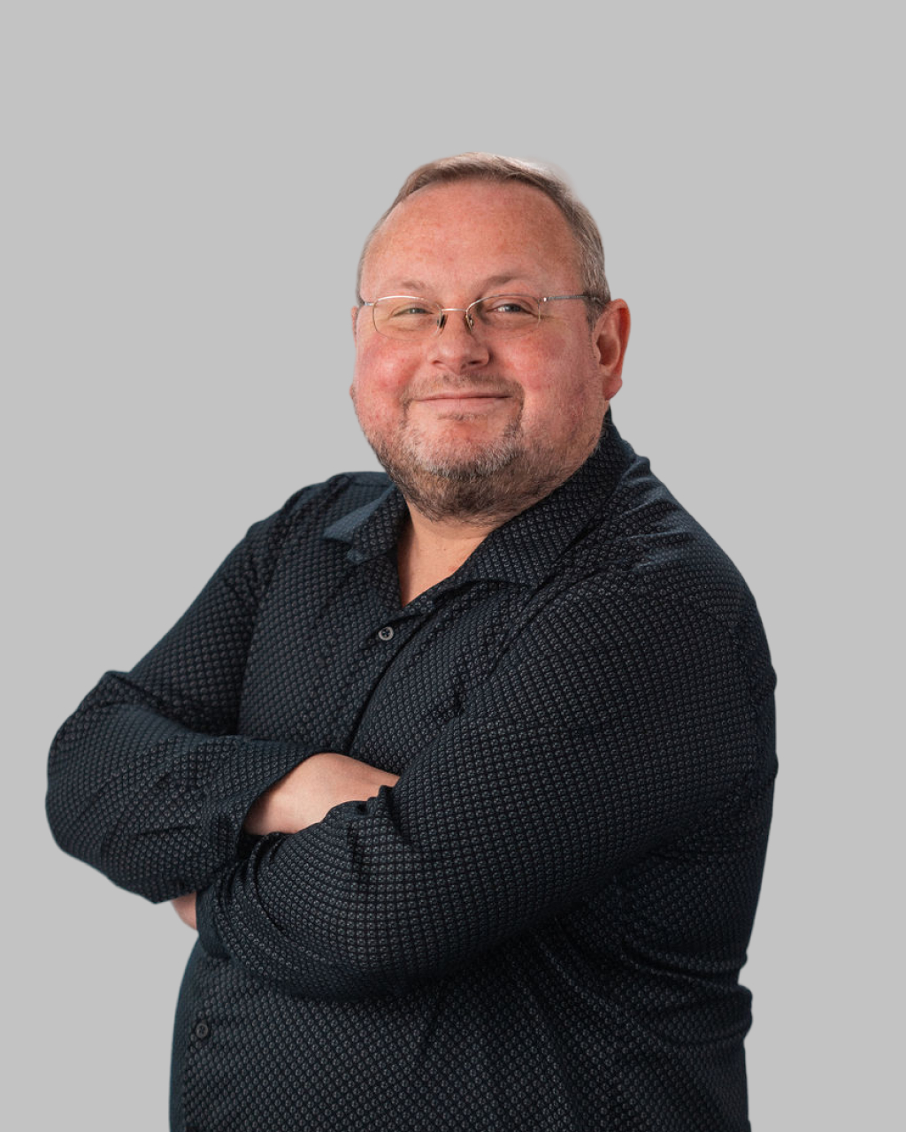 Francois Botha, a man with glasses and a beard, stands with arms crossed in a dark patterned shirt against a plain grey background.