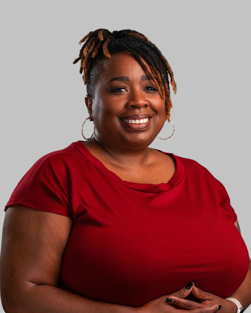 Kimberli D. Wright, a woman with short, twisted hair and hoop earrings, smiles at the camera in a red top against a plain gray background.