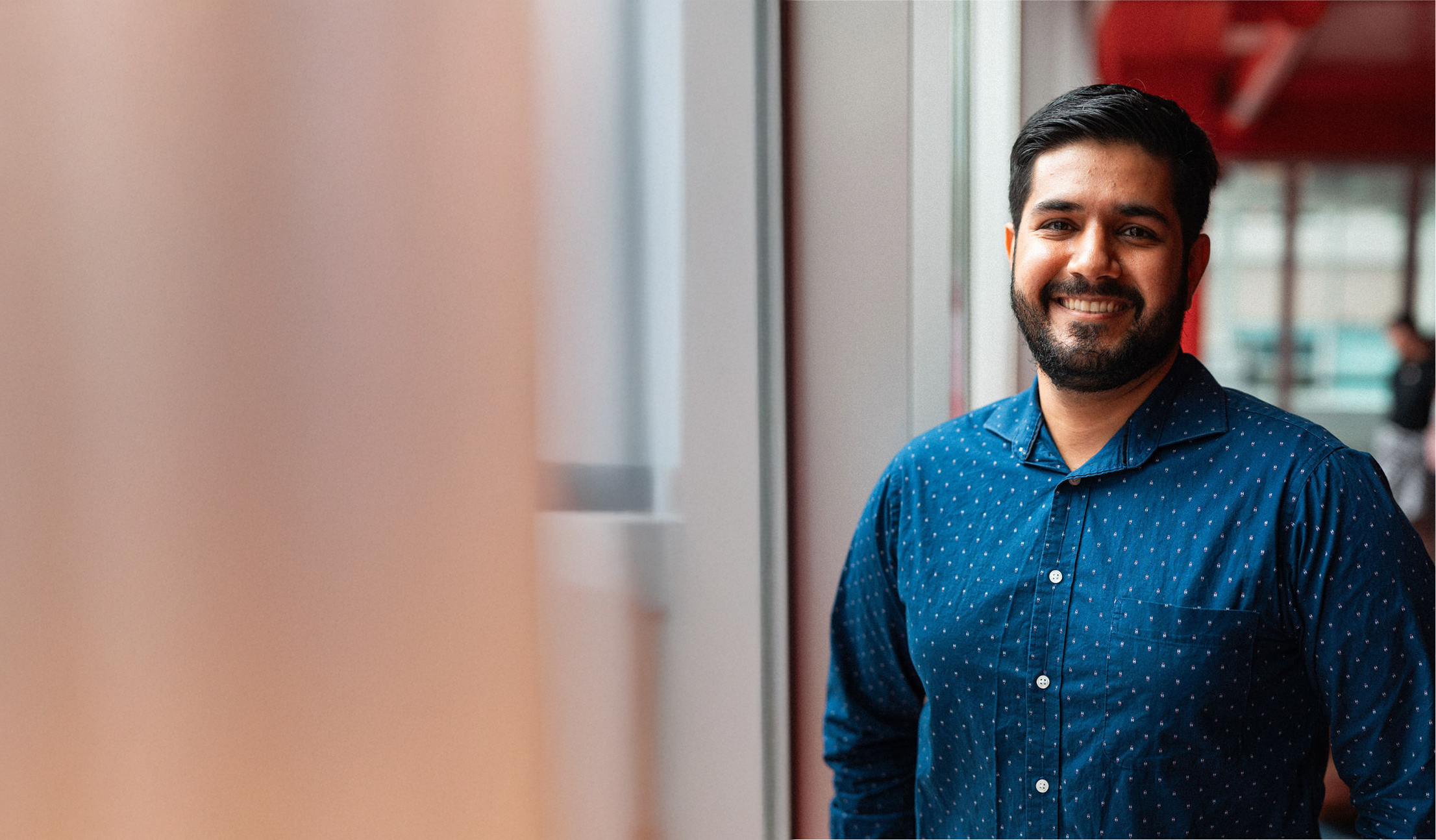 Male student stands by large window smiling at camera