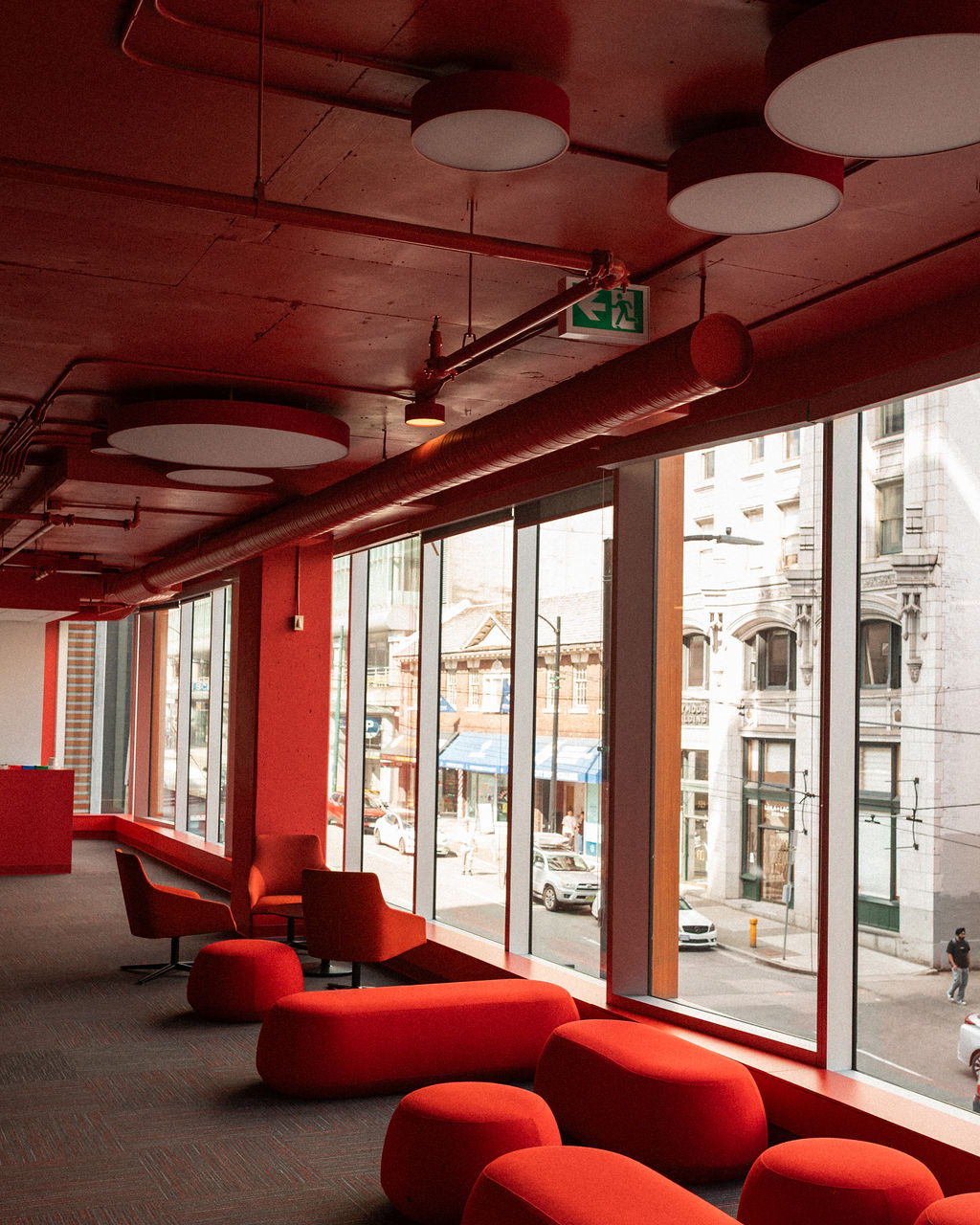 A modern lounge area with red furniture and ceiling, featuring large windows overlooking a city street with historic buildings.
