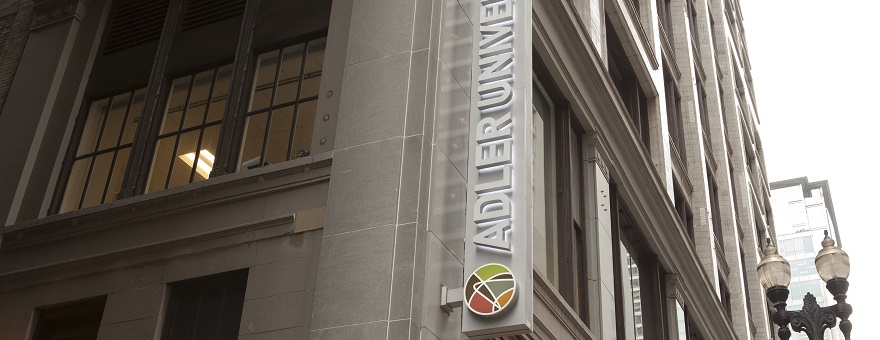 A vertical sign on a city building reads "Adler University" with the university's colorful circular logo at the bottom.