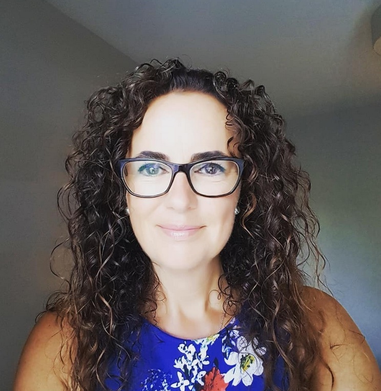 Portrait photograph of Anne centered in frame. She has dark curly hair and black-framed glasses.