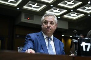 CSIS Director dressed in a blue suit, sitting behind a desk with a pensive look on his face.