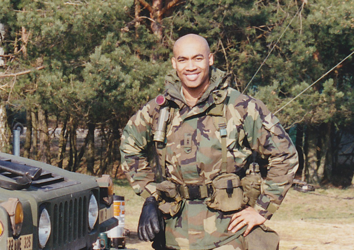 A person in military camouflage uniform stands outdoors next to a vehicle, smiling, with trees in the background—reflecting resilience and insights from military psychology.