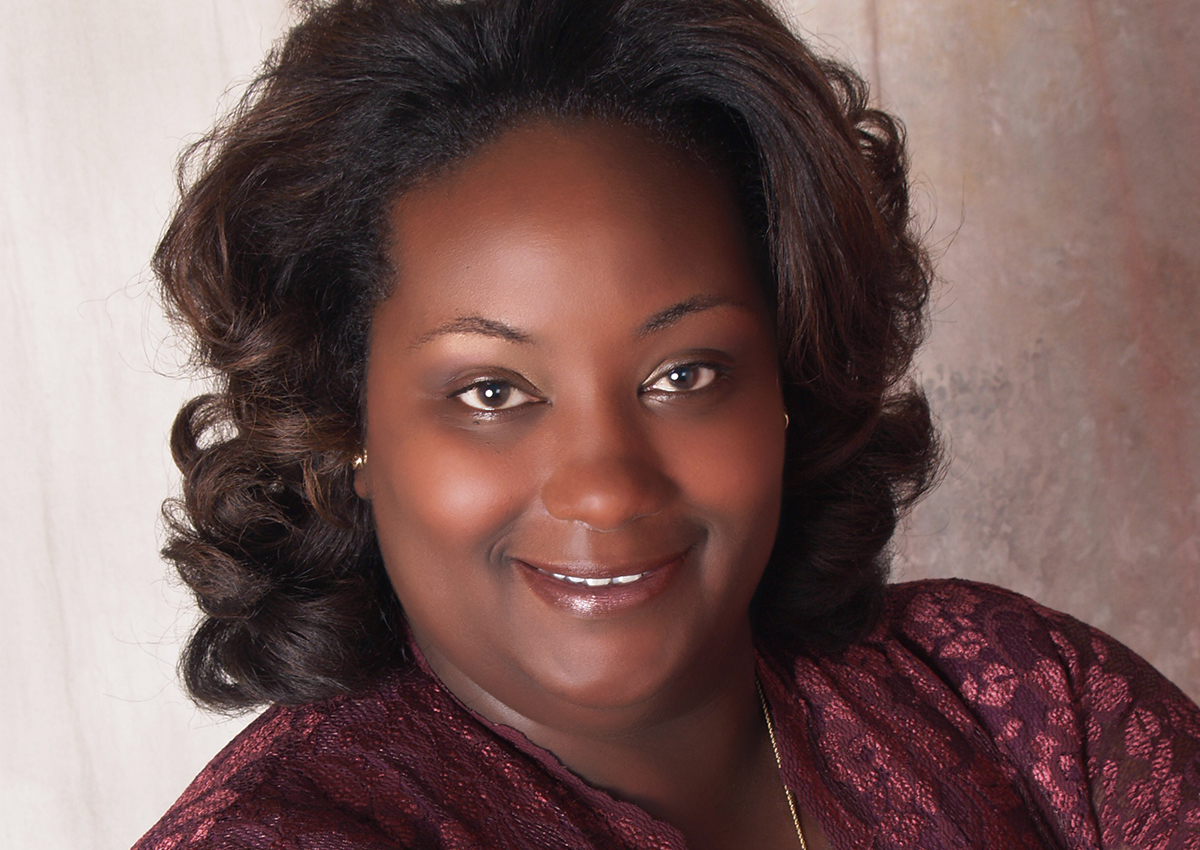 Cheryl Magee, a true Change Agent, smiles with shoulder-length curly hair and a burgundy lace top, posed in front of a neutral background.