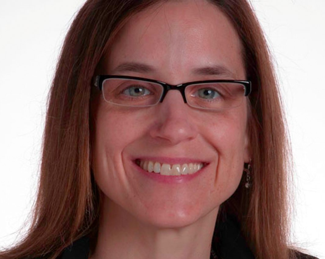 A woman with long brown hair and glasses, smiling at the camera against a plain white background, represents the overlooked stories of women on the autism spectrum and the frequent misdiagnoses they face.