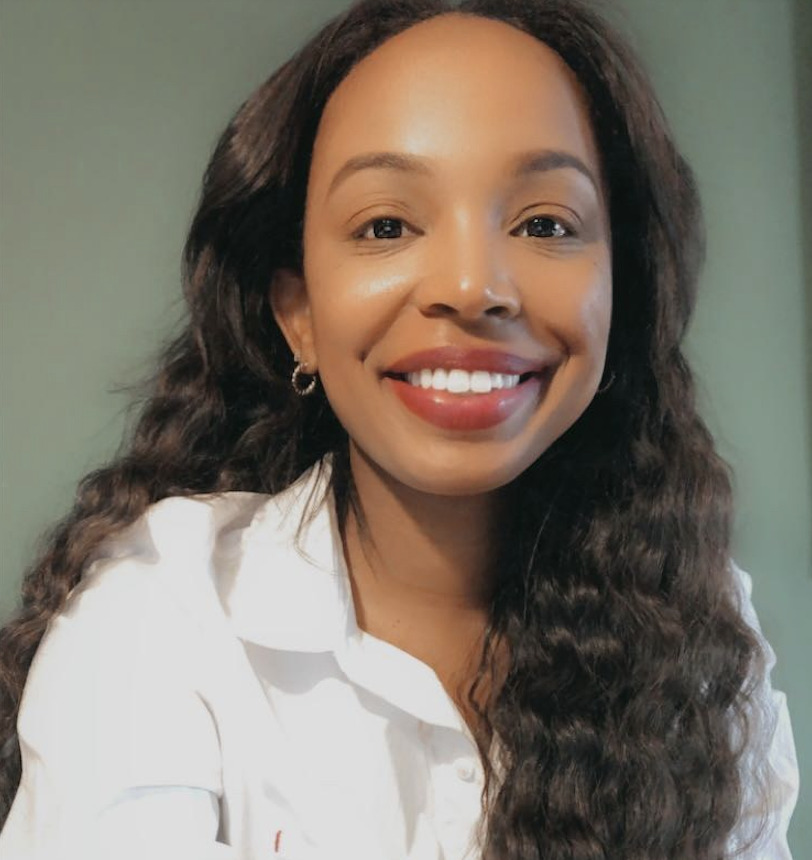 An Adler Student with long wavy hair and a white shirt smiles at the camera in front of a plain green background.
