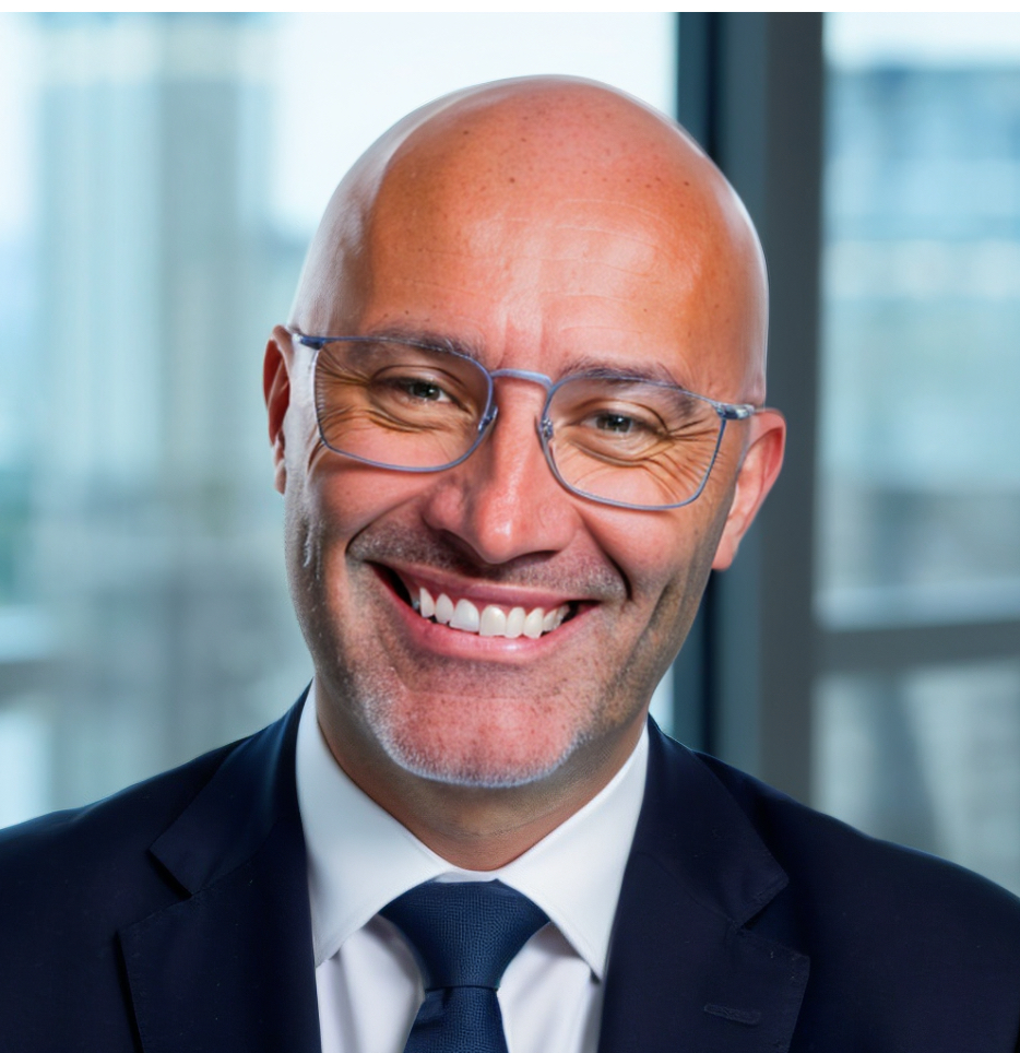 Dr. Jason Walker, core faculty in Industrial and Organizational Psychology, is a bald man wearing glasses and a suit, smiling in front of a blurred window background.