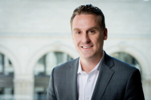 Man siting in front of building wearing a suit jacket