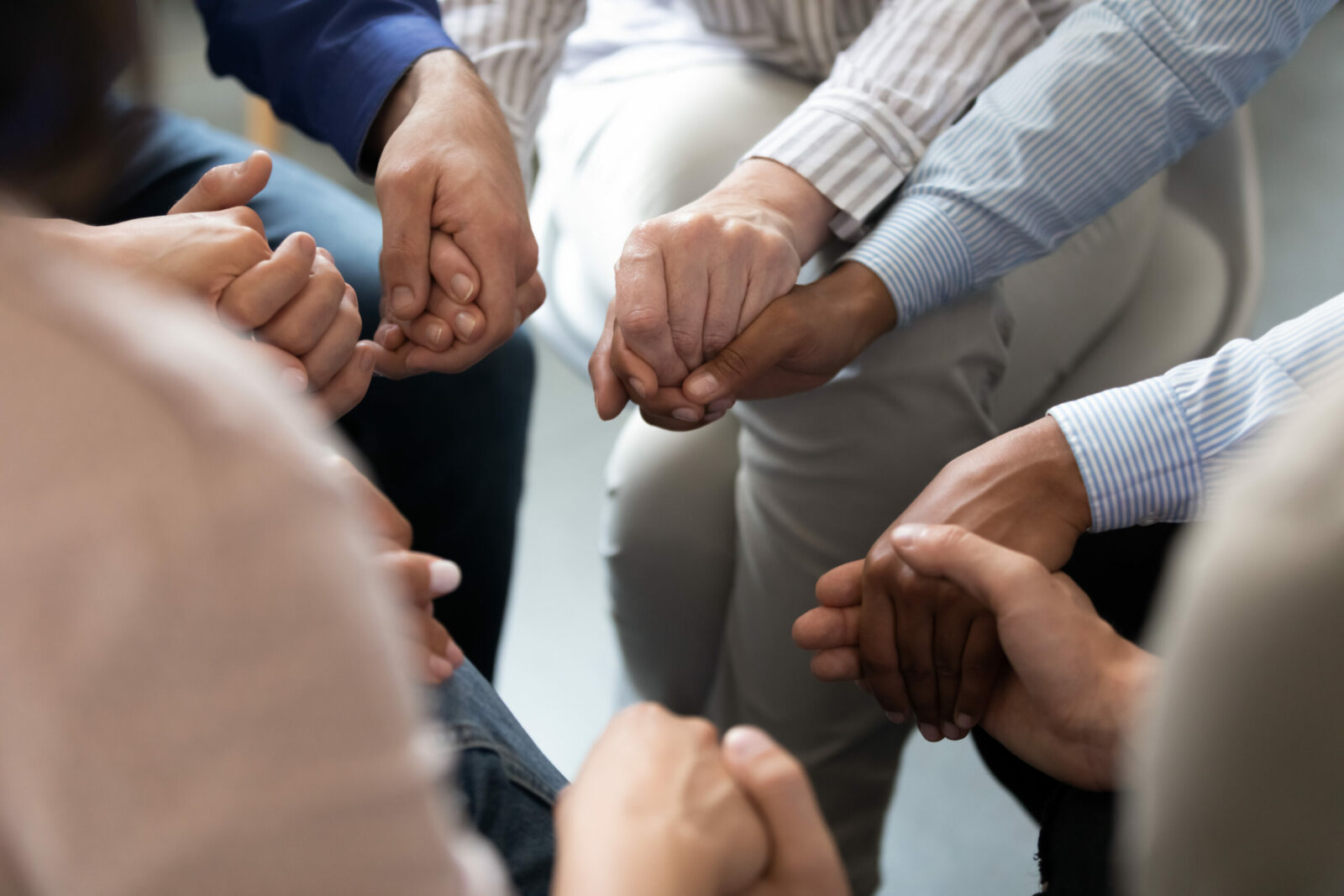 A group of people sit in a circle, holding hands in a gesture of support and unity, embodying a trauma-informed initiative led by peacemakers in Illinois correctional facilities.