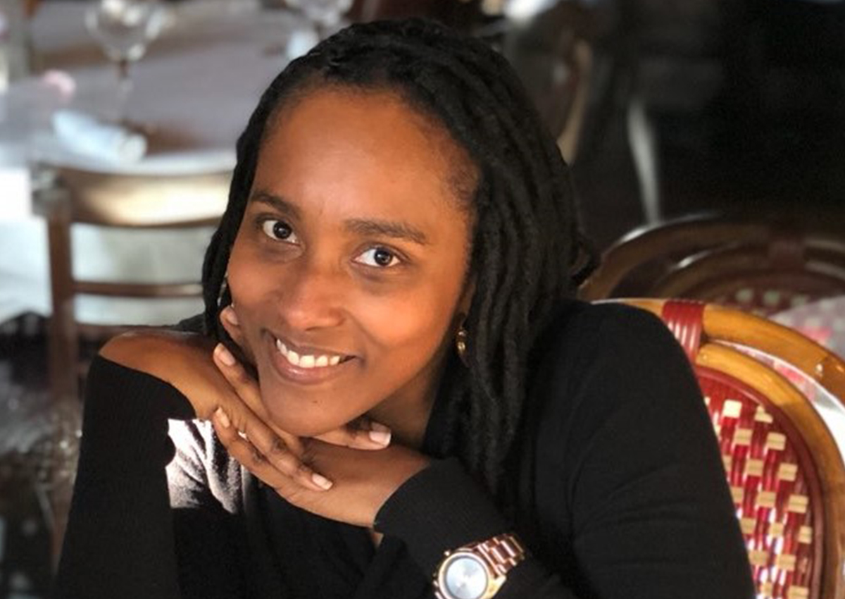 A woman with long braided hair rests her chin on her hands and smiles at the camera, showcasing the diversity of guests while seated at a table in a restaurant.