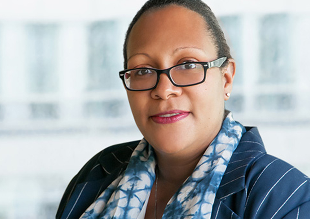 Dr. Dennis is sitting in front of a large window with a building blurred in the background. She is wearing a blouse and blazer.