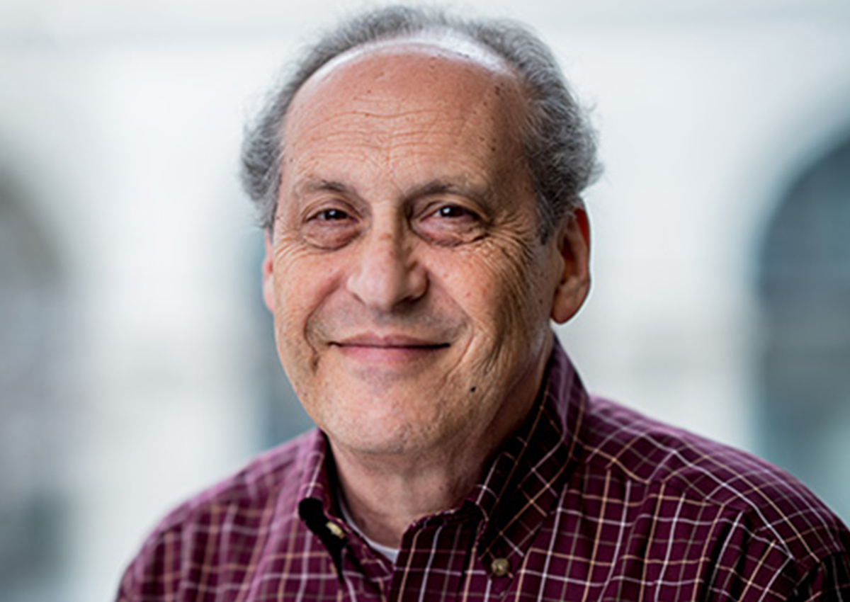 Dr. Rubin is sitting in front of a large window with a building blurred in the background. He is wearing a buttoned-up shirt.