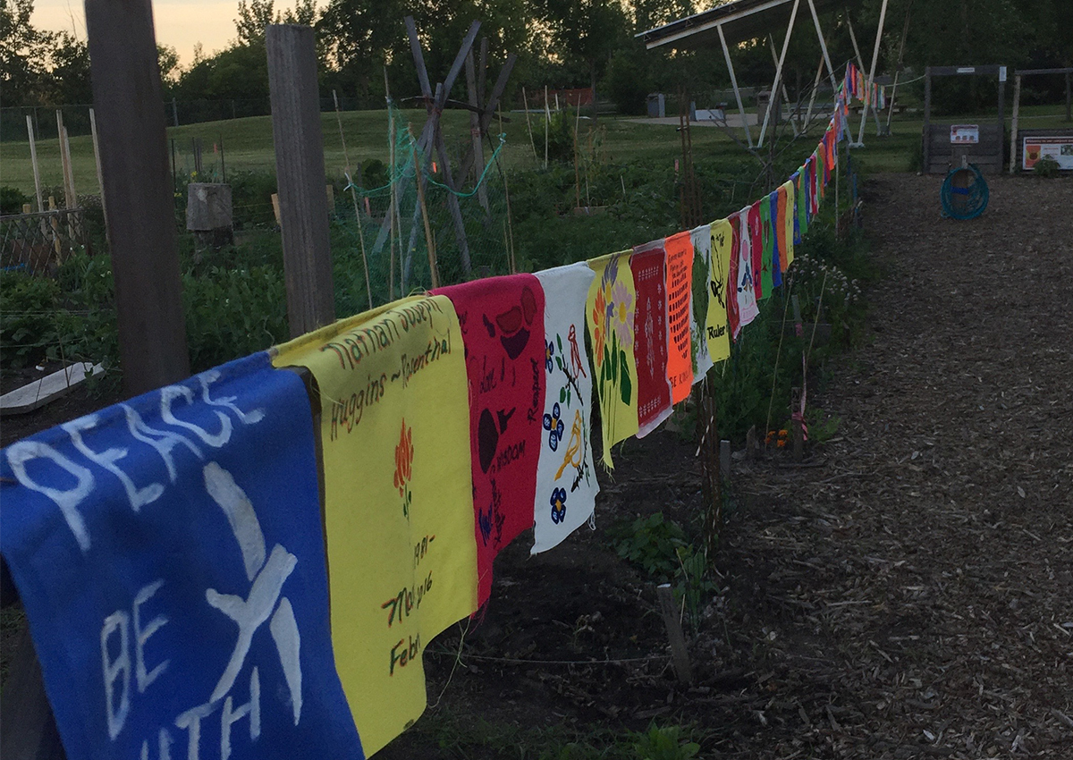 Colorful cloth banners with various designs and messages hang on a line between wooden posts, celebrating community spirit on the front lines of this vibrant garden setting.