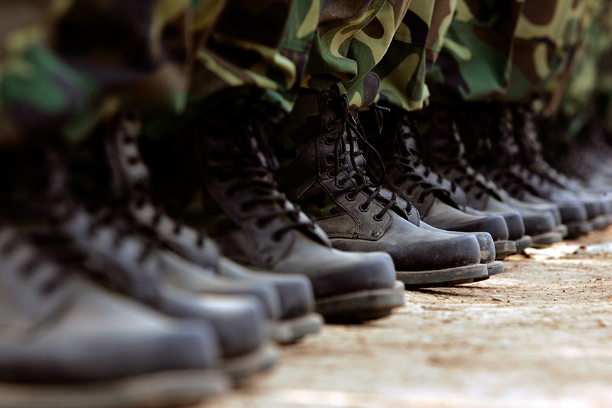 Una fila de personas con botas militares negras y pantalones de camuflaje, alineadas en formación sobre una superficie de hormigón.