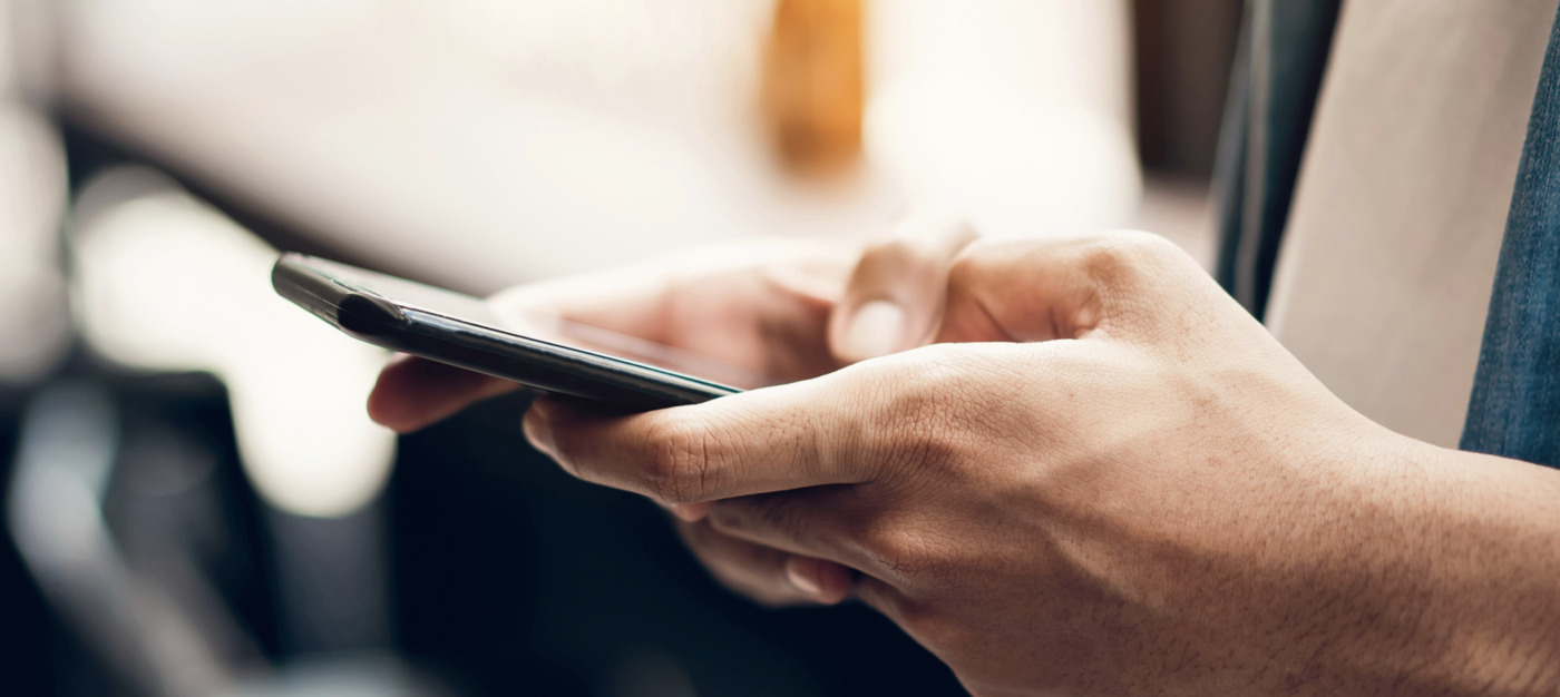 Close-up of a person’s hands holding and using a smartphone, highlighting digital access to Community Mental Health Services, with a blurred background.