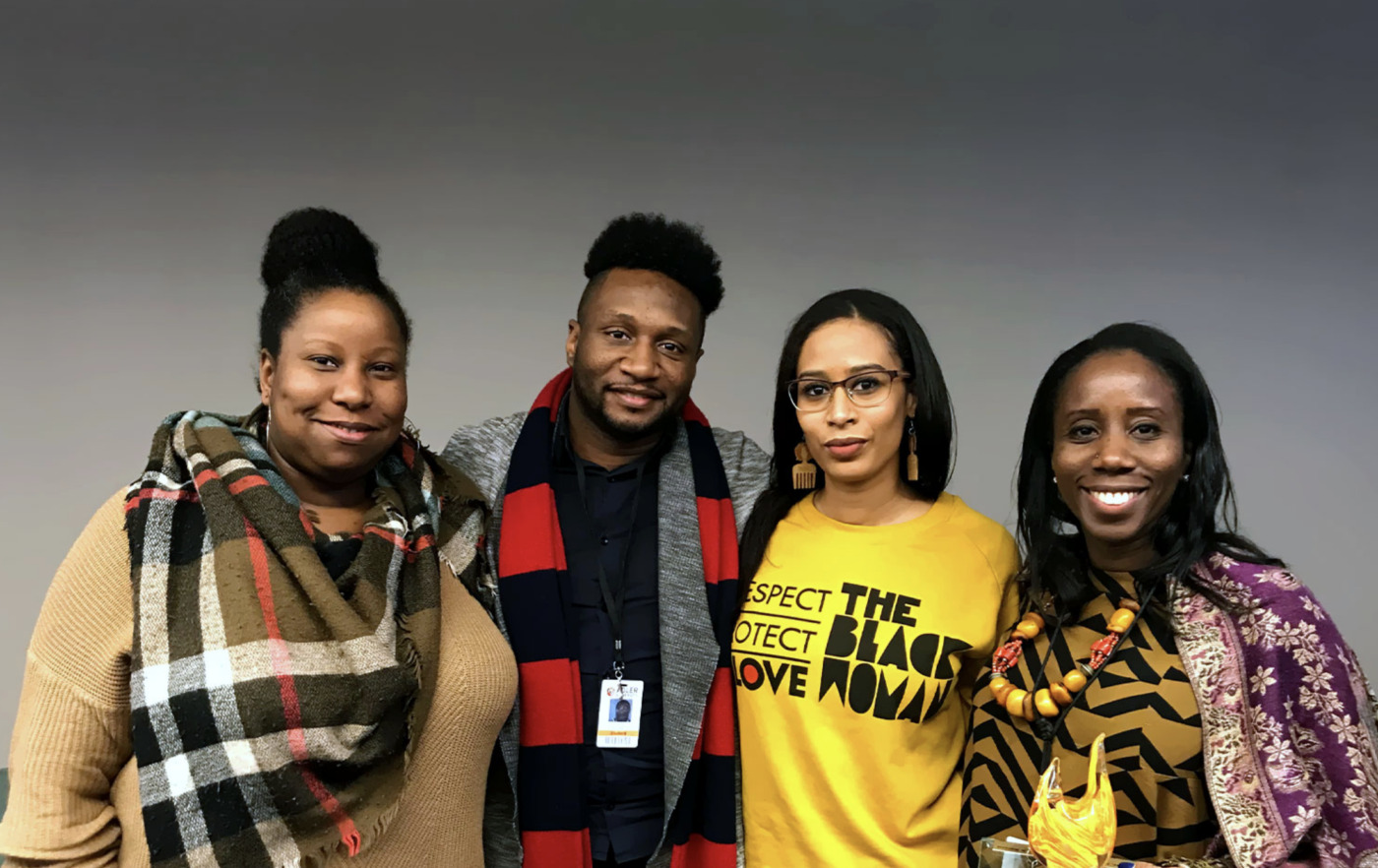 Four people stand side by side, smiling at the camera against a plain background. One person, Nataka Moore—a true Change Agent—wears a yellow "The Black Love Now" shirt.