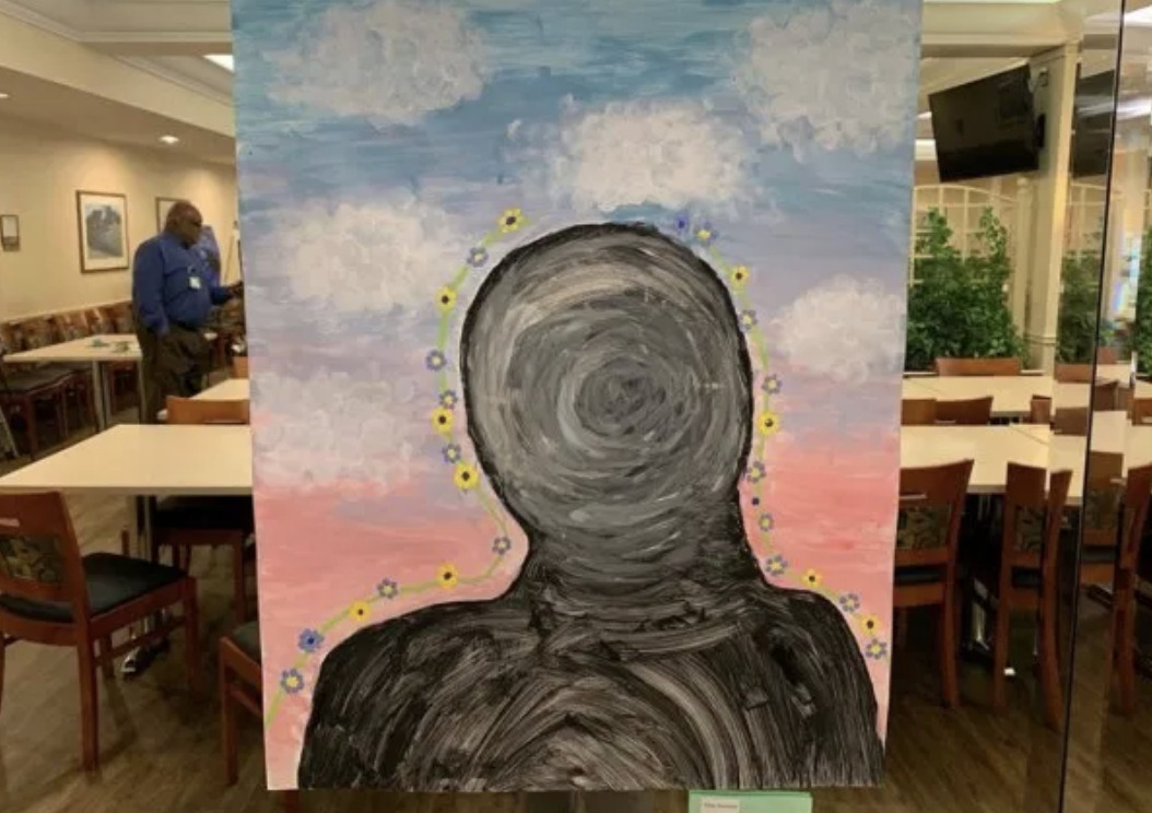 A painting of a faceless, dark figure with circular patterns, outlined by small flowers, against a pastel sky with clouds; evokes art therapy and invites patients to feel seen when displayed in a dining area.