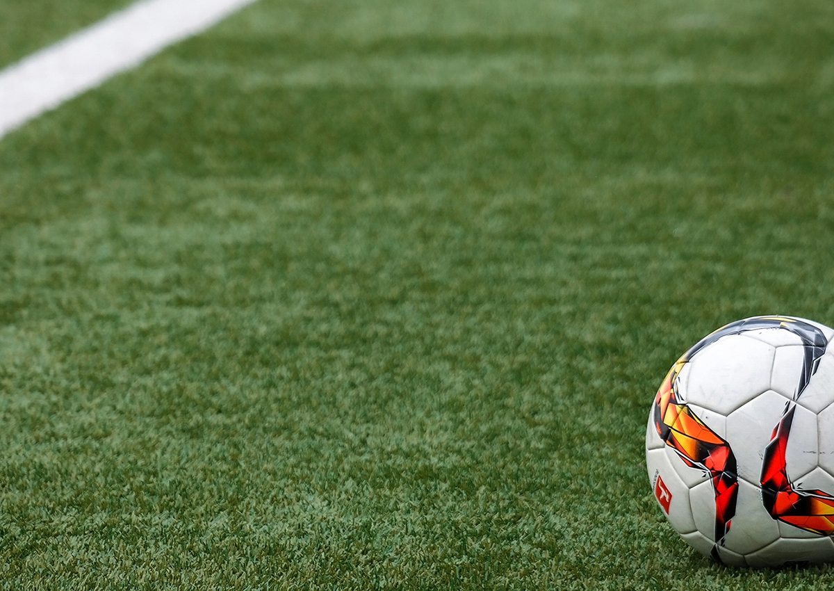 A soccer ball with a red and yellow pattern rests on green artificial turf near a white sideline, ready for winning moments inspired by the World Cup.