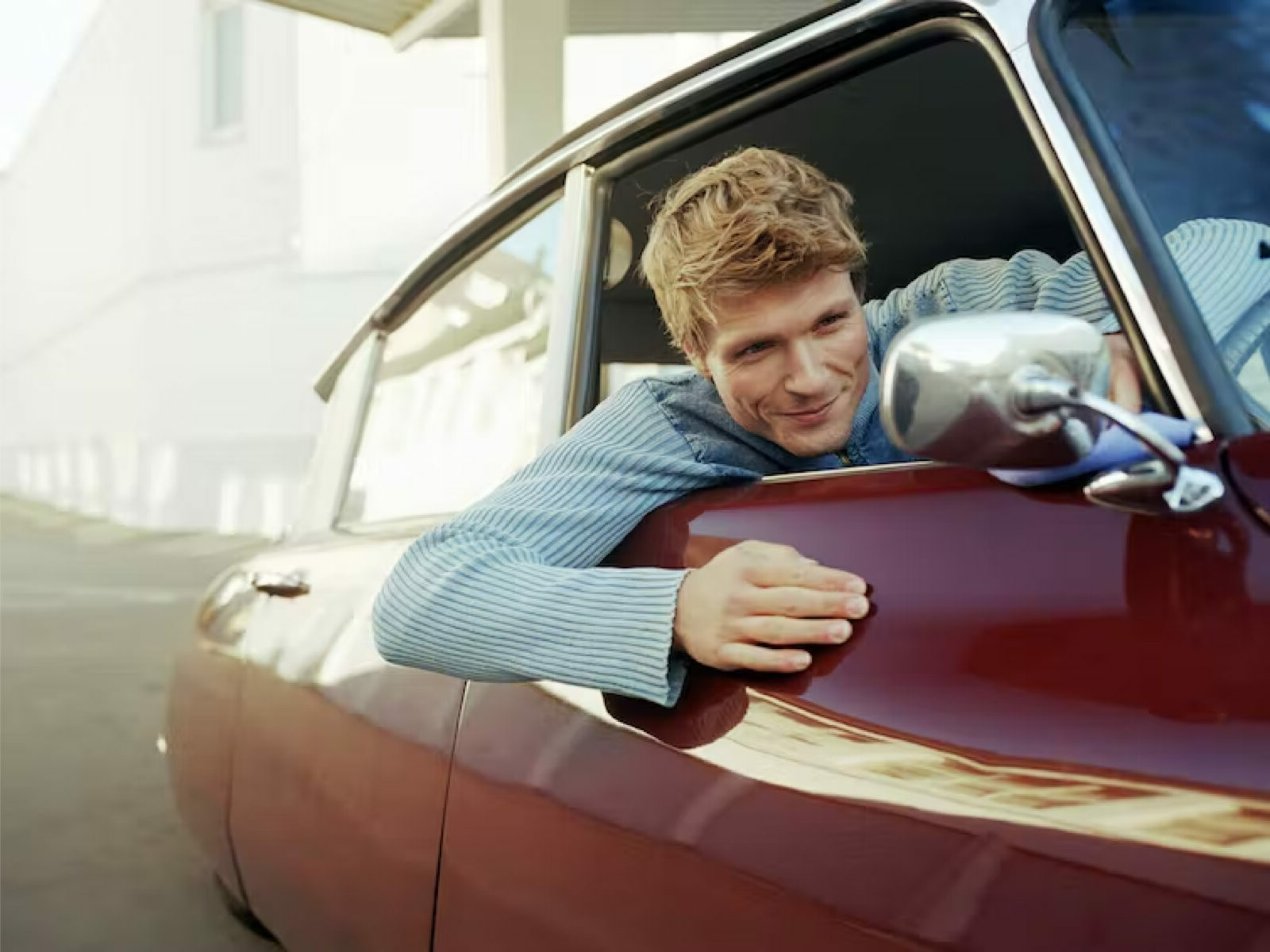 Man looking out car window into his side mirror.