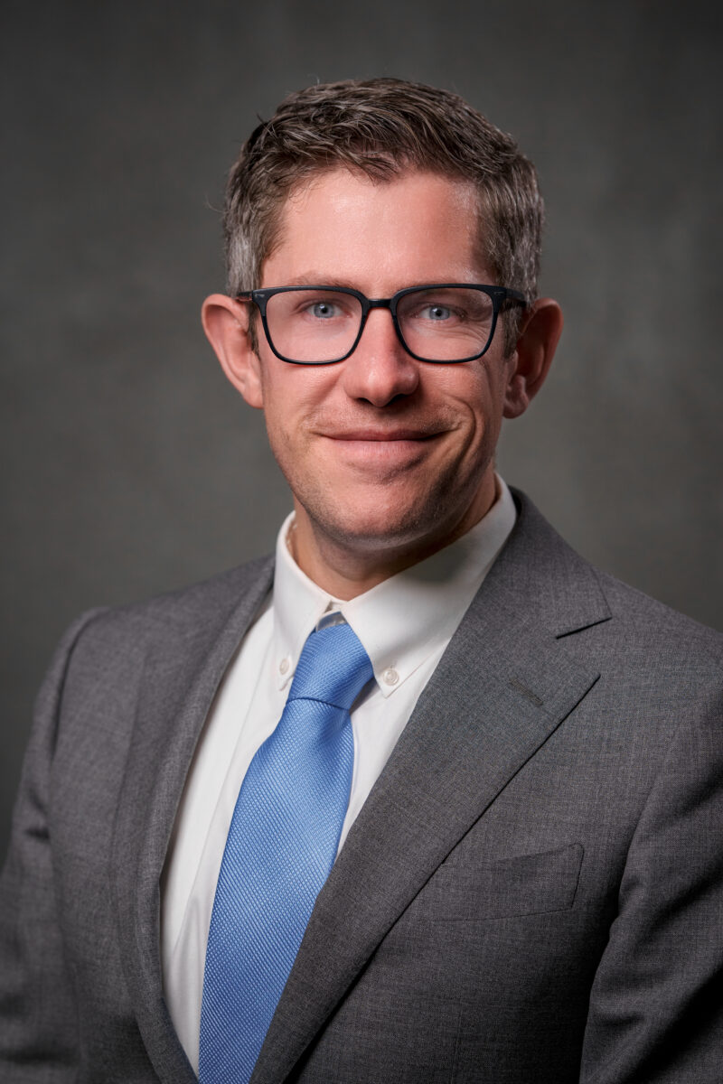 Man in grey suit and blue tie smiling