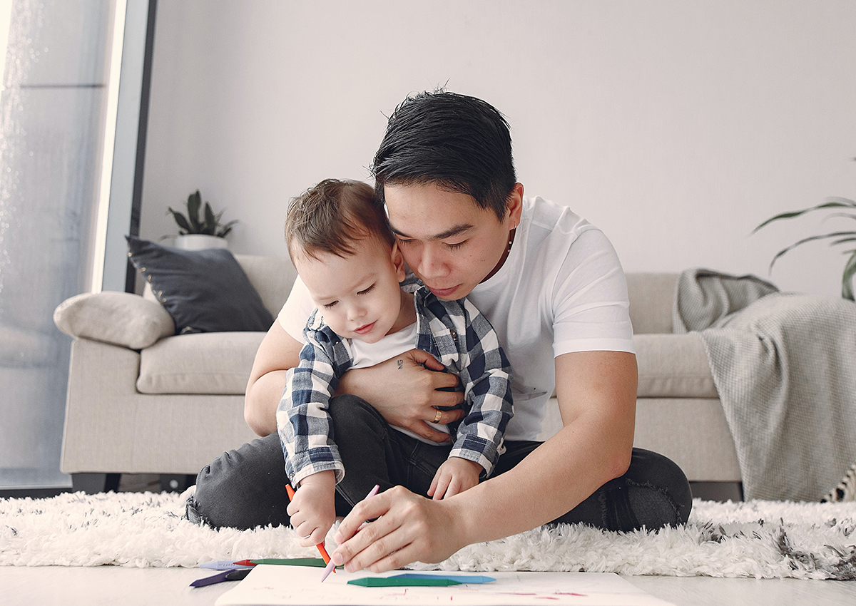 An adult and child sit on the floor drawing together, with coloring supplies scattered in front of them—capturing a cozy moment of art therapy in a welcoming living room setting.