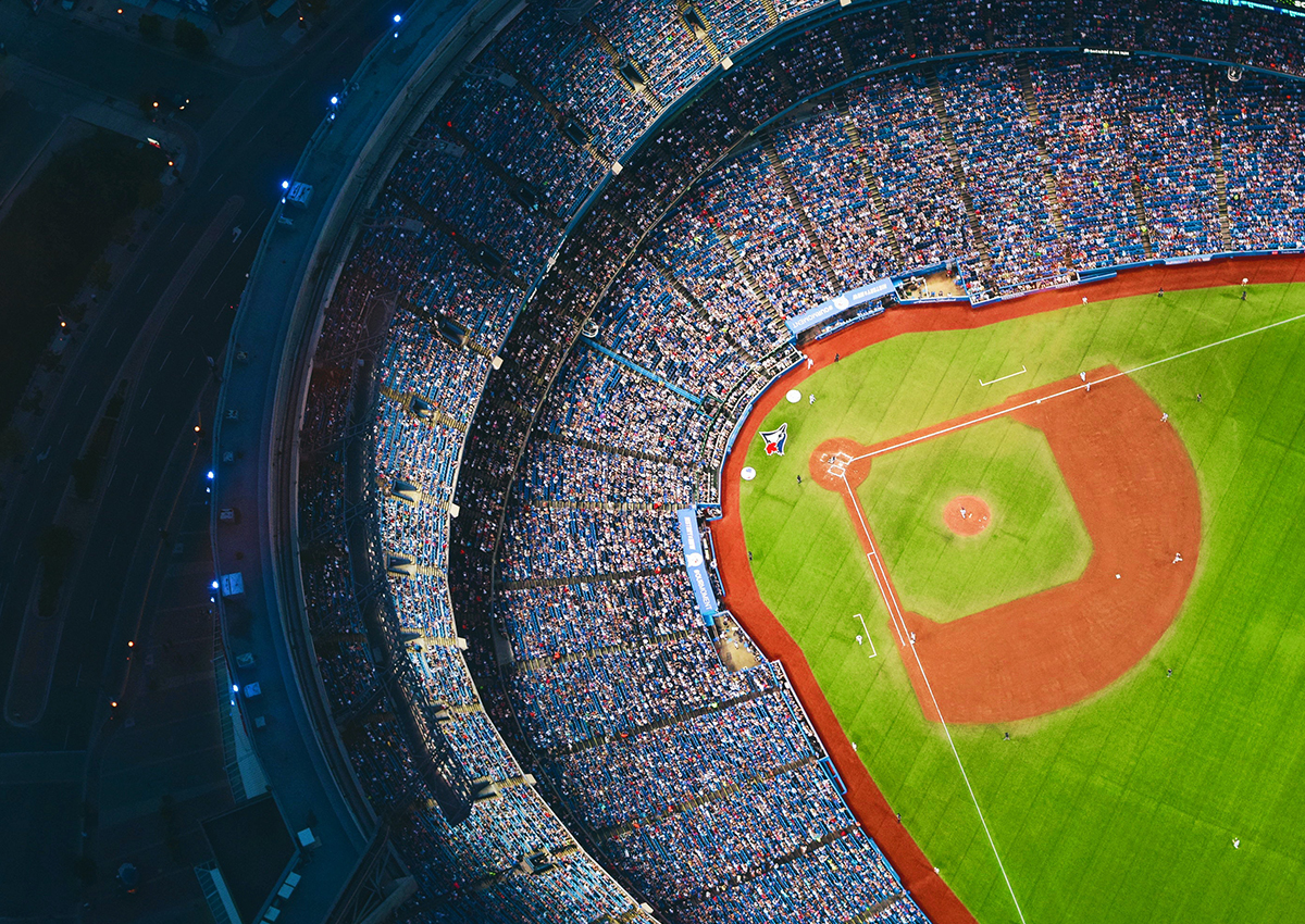 Aerial view of a baseball stadium filled with spectators, including students and sport enthusiasts, showing the field, bases, and surrounding stands during a game.