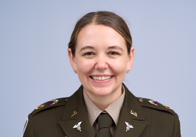 A person in a U.S. military uniform with medical insignia is smiling at the camera against a plain light blue background, identified as Amy Thrasher, Psy.D.