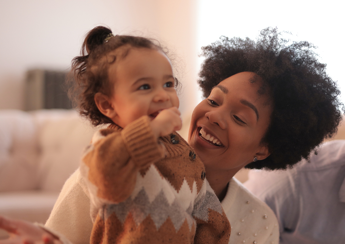 A woman smiles at a young child wearing a brown patterned sweater as they sit together indoors, strengthening relationships through nurturing moments.
