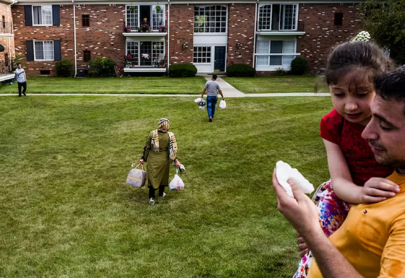 A family walks across a grass lawn with their belongings.