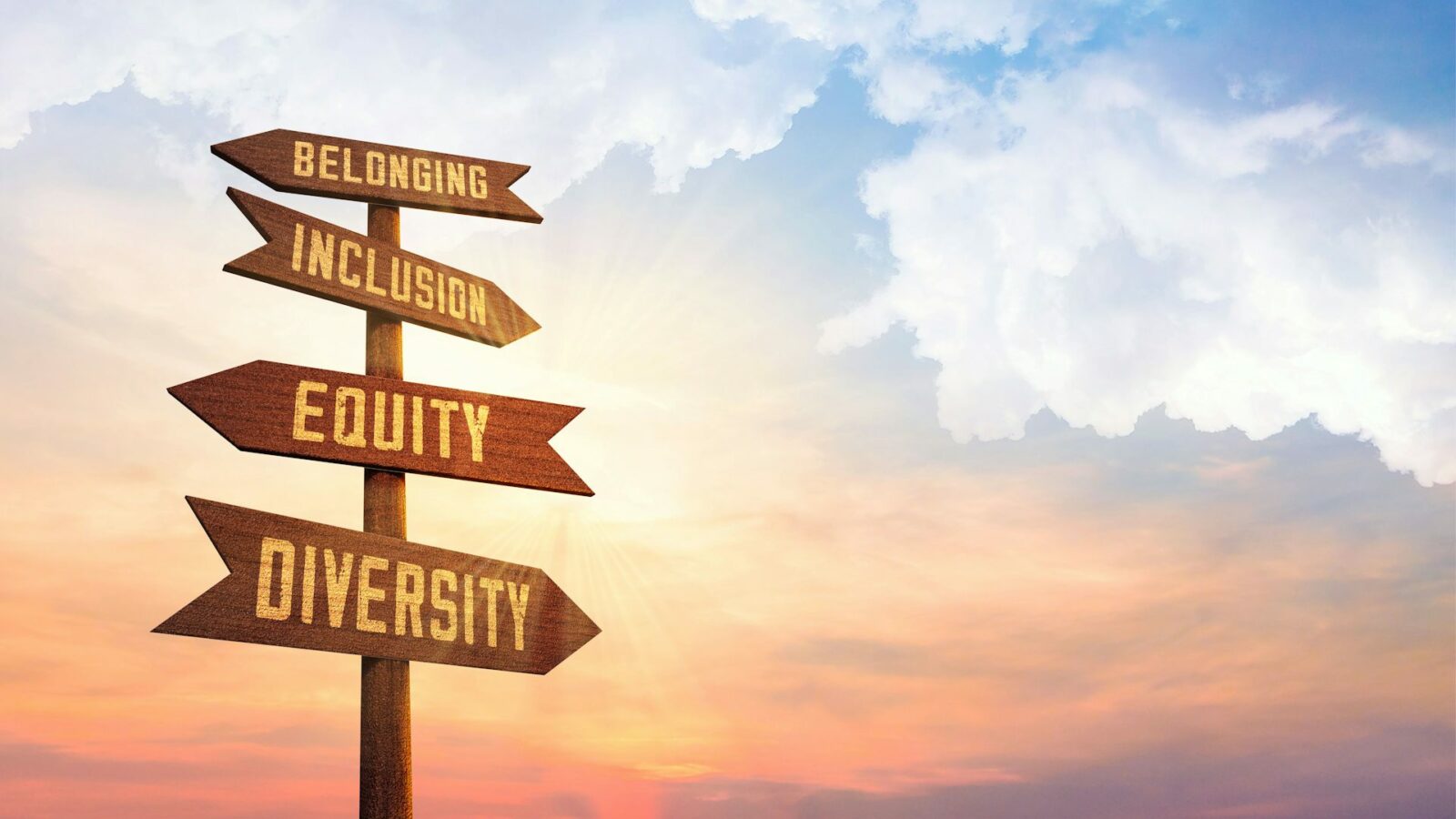 A sign with arrows and text on each arrow, against a backdrop of an orange sky.