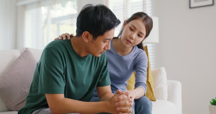 A woman comforts a man as they sit on a couch