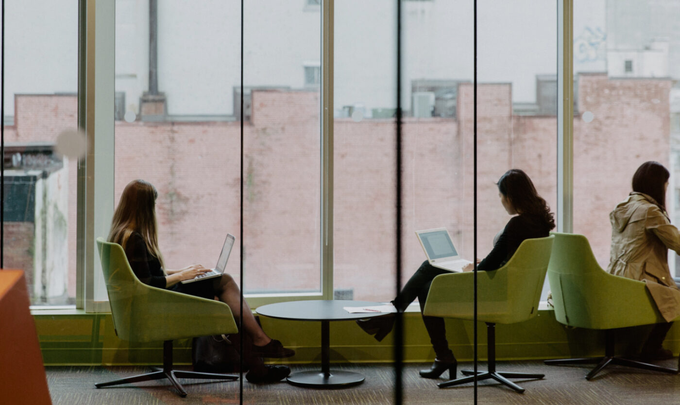 Three people sit on green chairs by large windows, working on laptops and facing away from the camera in a modern office space at Adler University, home to one of the best in Canada counselling psychology programs.