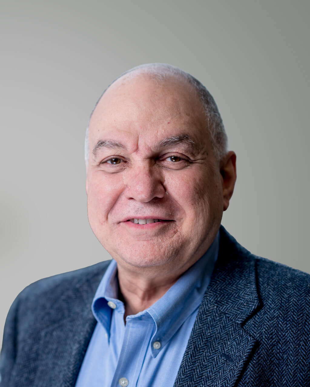 A middle-aged man with short gray hair wearing a blue dress shirt and a gray blazer, smiling at the camera against a plain background.