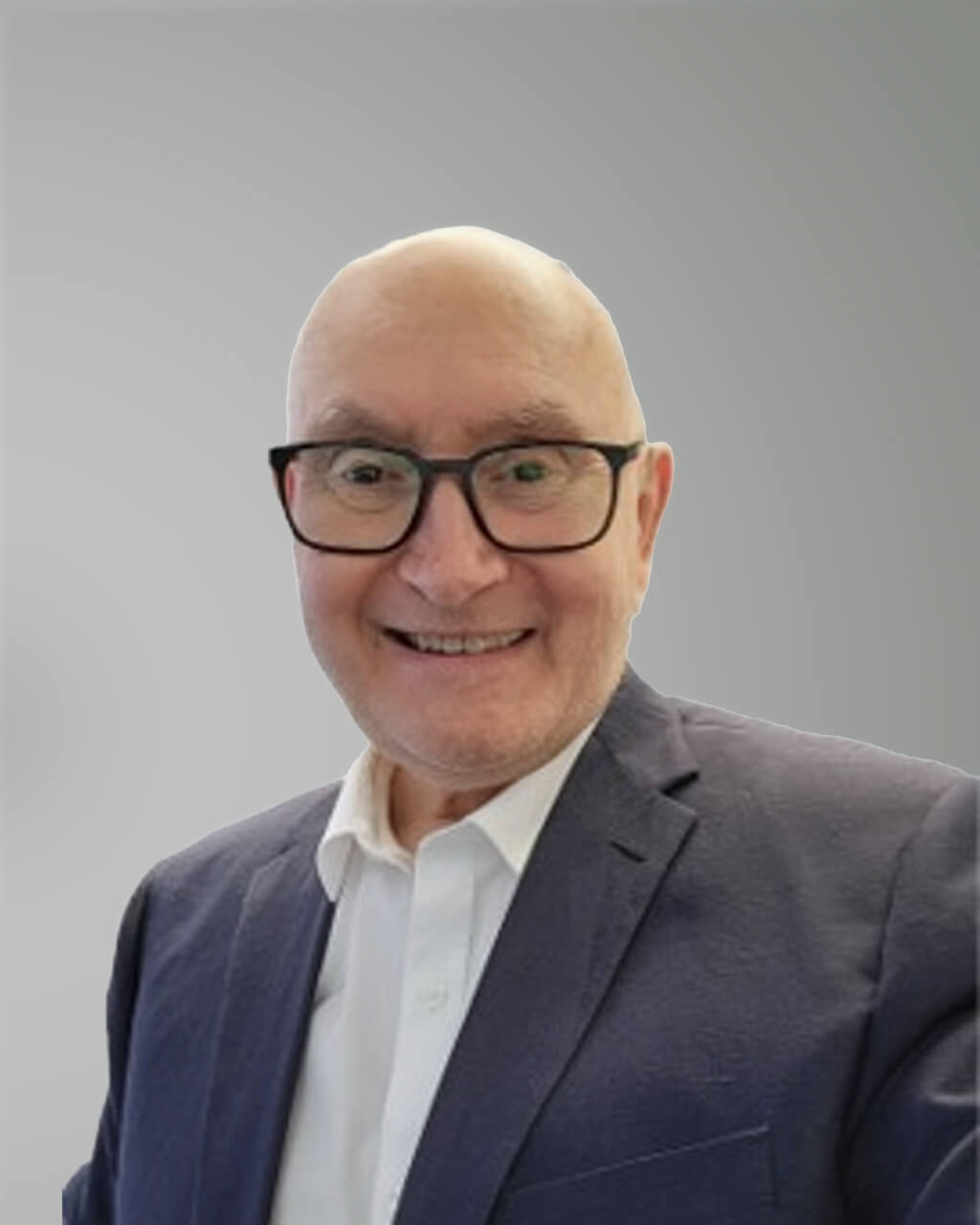 A man wearing glasses, a white shirt, and a navy blazer is smiling in front of a plain gray background.