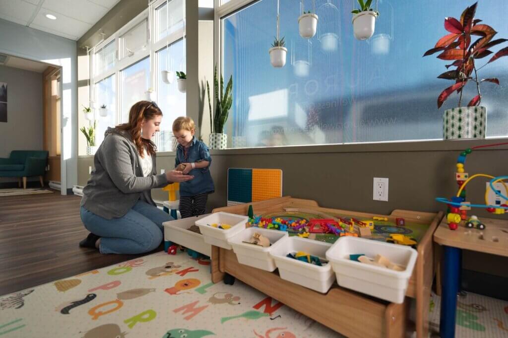 An adult and a child interact in a brightly lit playroom with toys, bins, and educational mats on the floor, as Stephanie Leithead’s Arctic-inspired decor brings an enchanting aurora of color to the space.