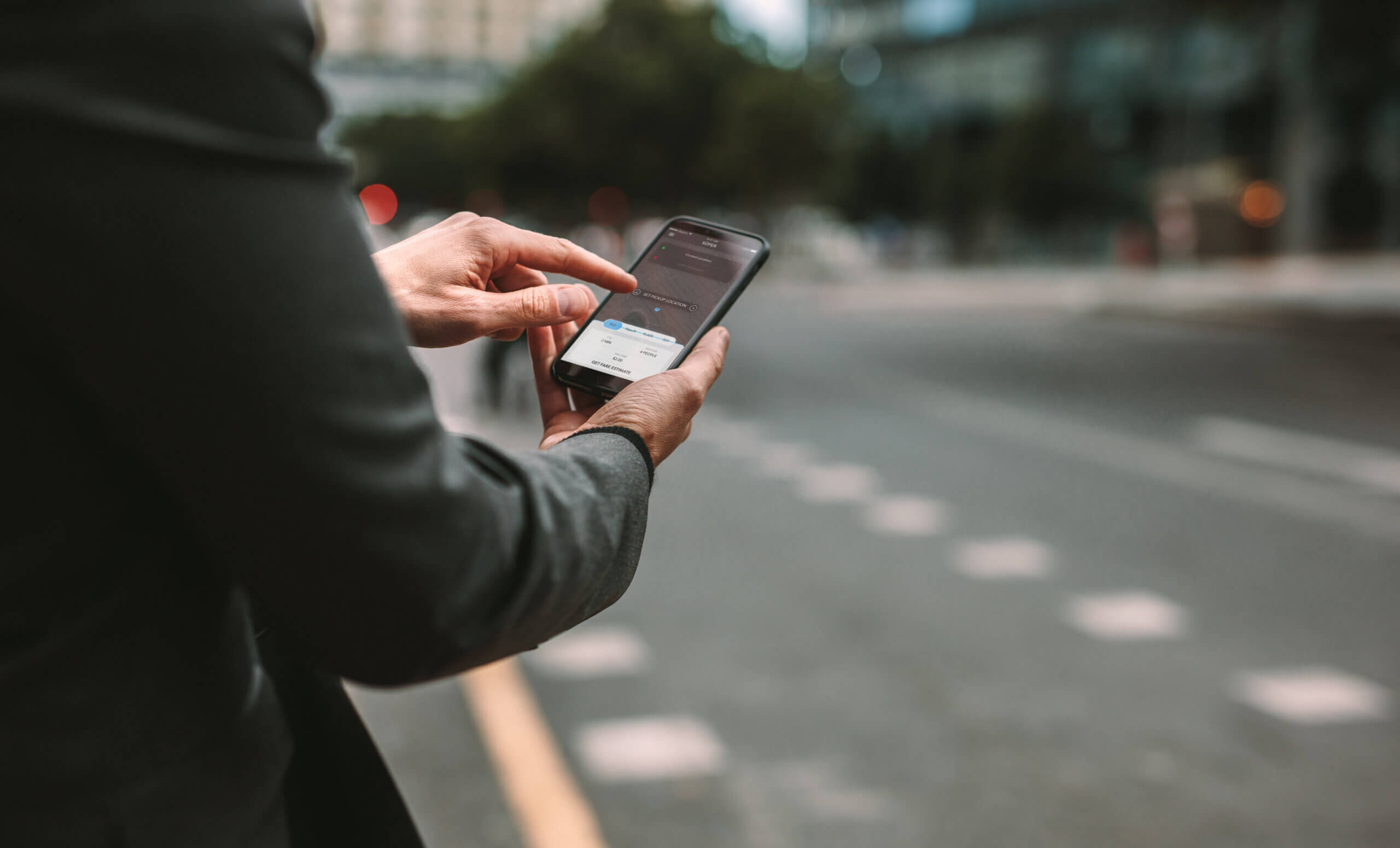 Person in a suit stands on a city street using a smartphone, possibly researching tips for relocating to Chicago, with one hand holding the phone and the other hand touching the screen.