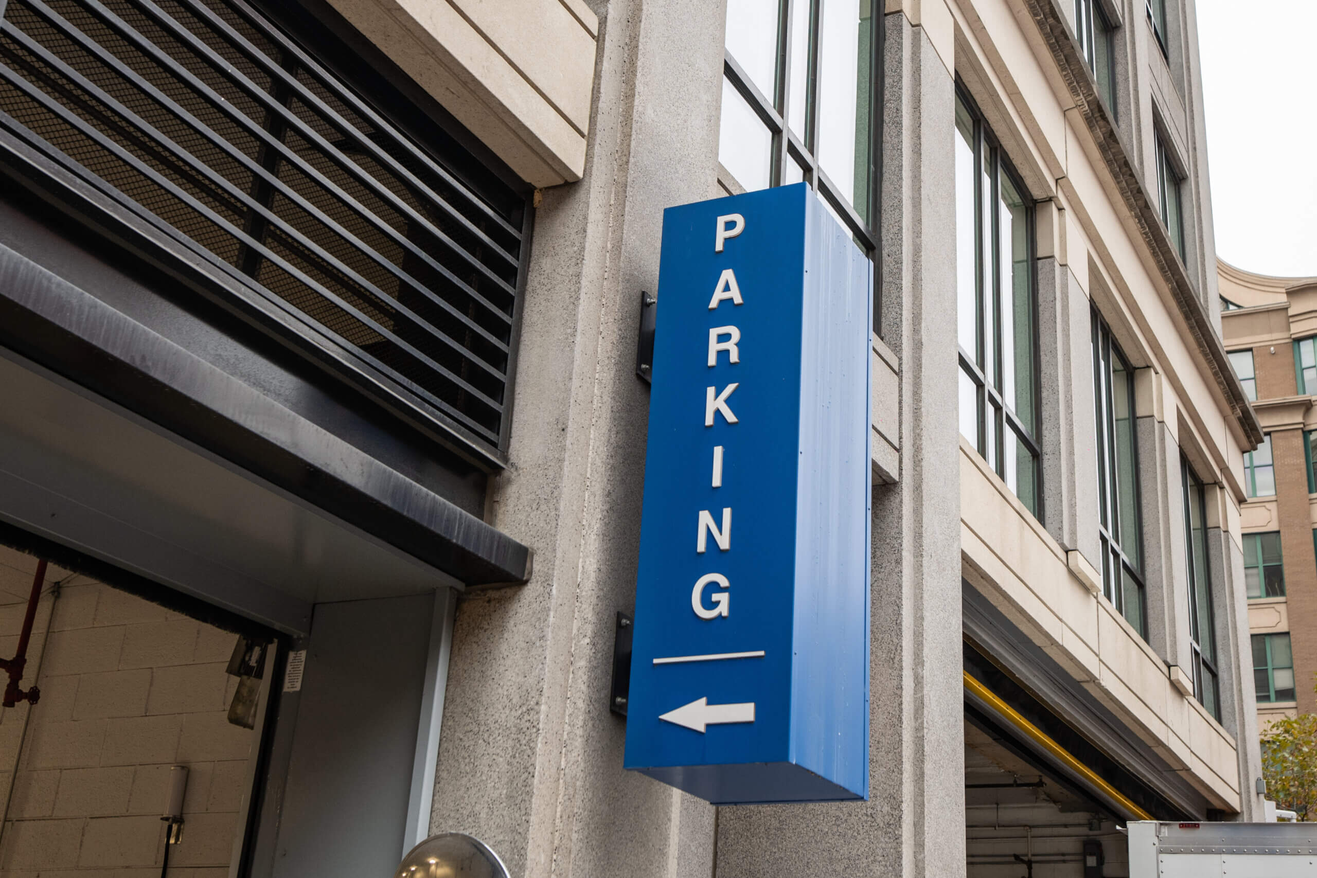 A blue vertical sign with "PARKING" and a left-pointing arrow is mounted on the side of a building—a familiar sight when relocating to Chicago.